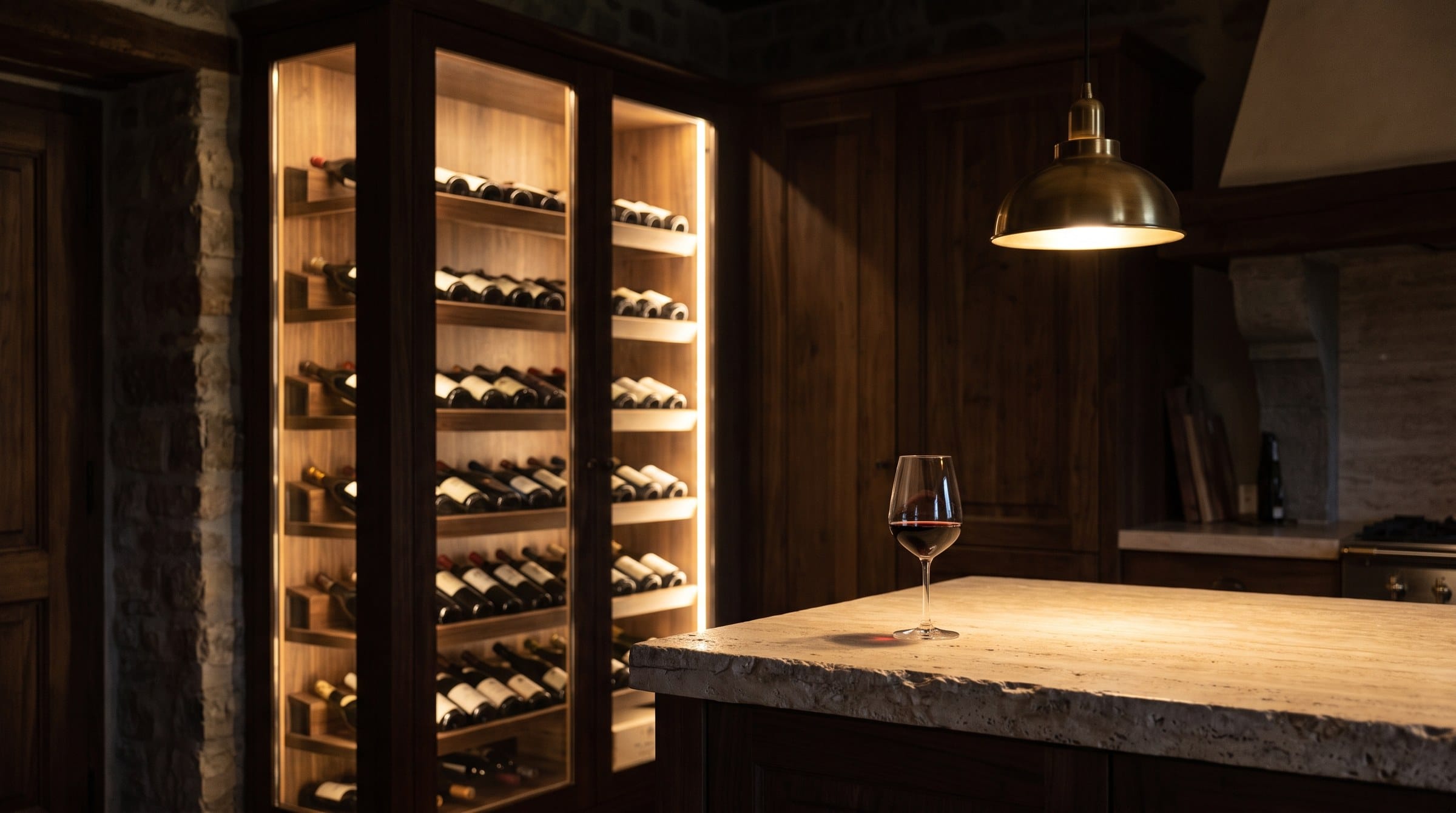 A wine climate cabinet glowing in dark cabinetry beside a travertine island