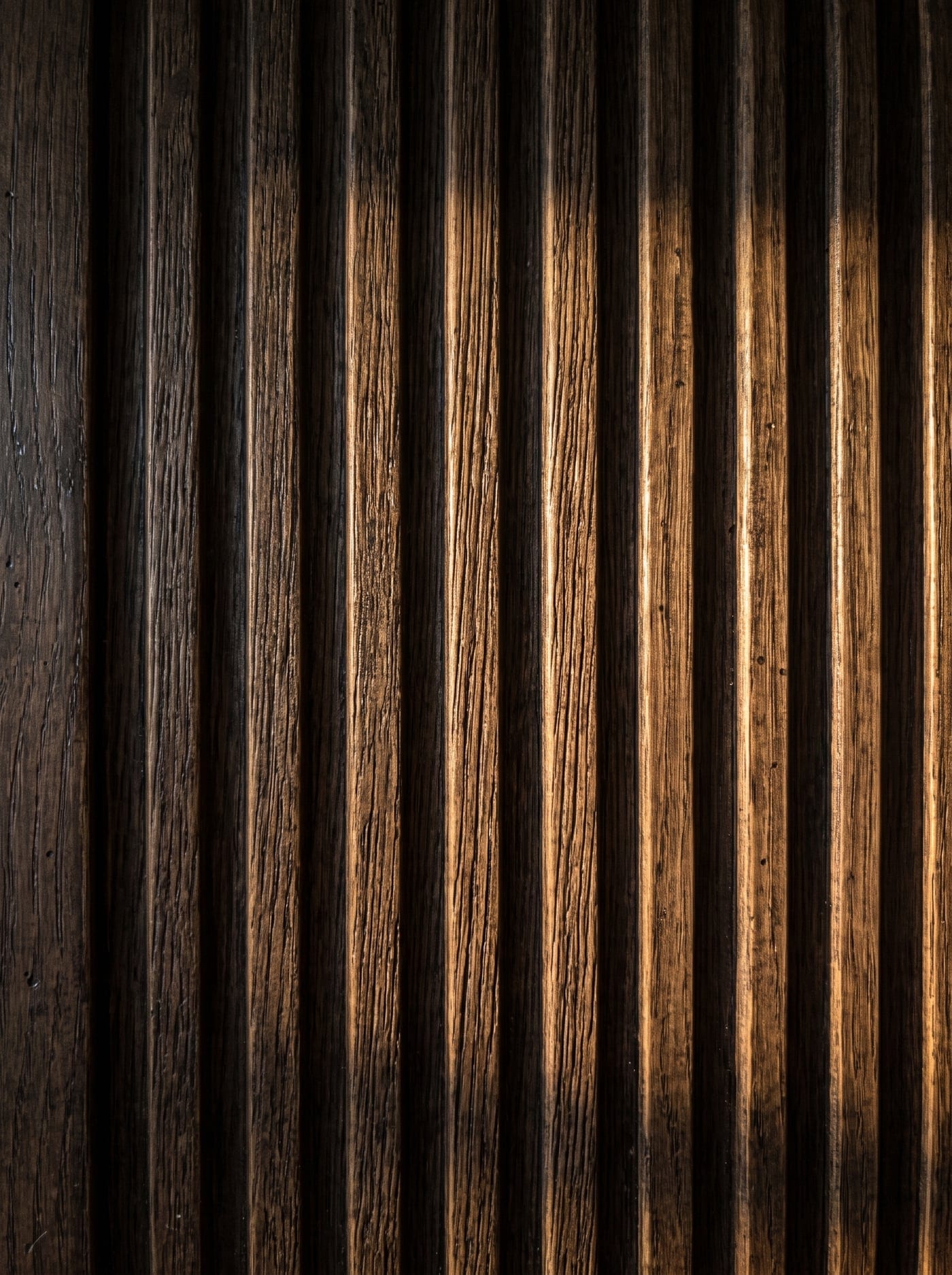 Macro study of a deeply fluted dark oak panel casting rhythmic shadows